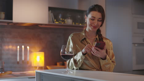 woman relaxing with a glass of wine and smartphone in a cozy kitchen