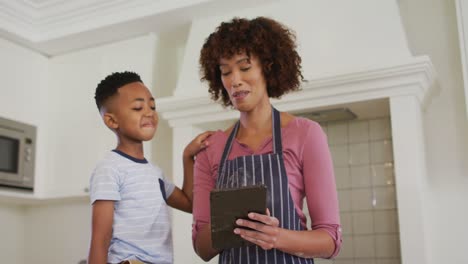 African-american-mother-and-son-in-kitchen-cooking,-looking-at-tablet