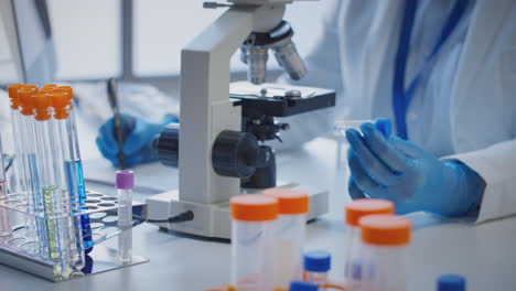primer plano de un trabajador de laboratorio que lleva a cabo investigaciones utilizando un microscopio con un tubo de ensayo etiquetado alfa