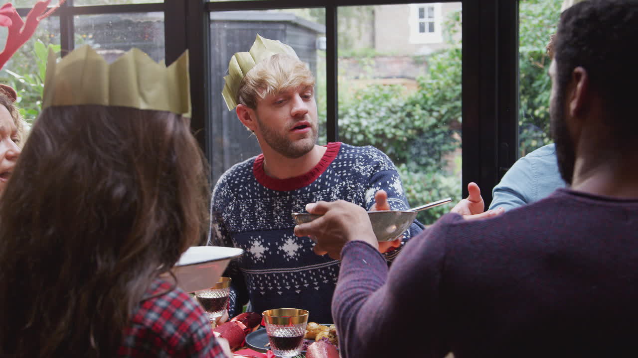 집에서 식탁 주위에 앉아 크리스마스 저녁 식사를 함께 즐기는 친구 그룹