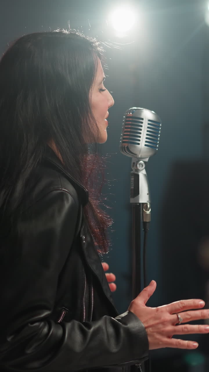 vista cercana de un cantante con una chaqueta de cuero negra actuando apasionadamente con un micrófono vintage contra un fondo gris. la cara expresiva del cantante y los gestos de las manos
