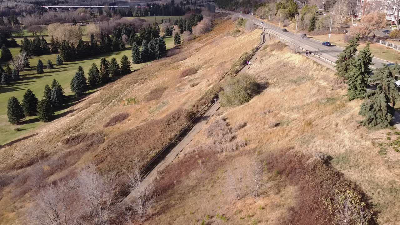 1-4 vuelo aéreo sobre el campo de golf del río del valle de la ciudad junto a un parque sin arreglar mientras una pareja se distancia socialmente de los demás caminando por el camino pavimentado camino de hormigón por la comunidad residencial oradside