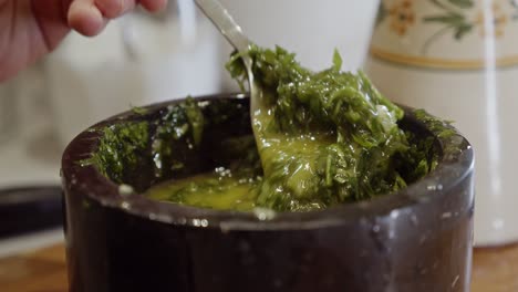 stirring with a metal spoon a healthy sauce with herbs in a ceramic black bowl