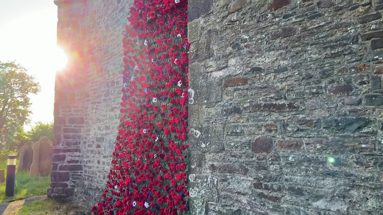 Giant Poppy Remembrance Wreath Stretching Up Church Wall at Sunset as Camera Pans Up Revealing Tall Building with Cloudy Sky. Part of VE Day Commemorations.