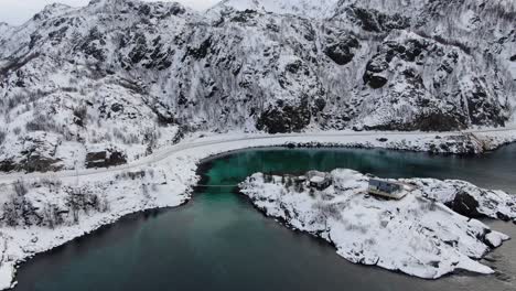 Drone-view-in-Tromso-area-in-winter-flying-over-a-hanging-wooden-bridge-to-an-island-with-a-clear-blue-sea-in-Norway