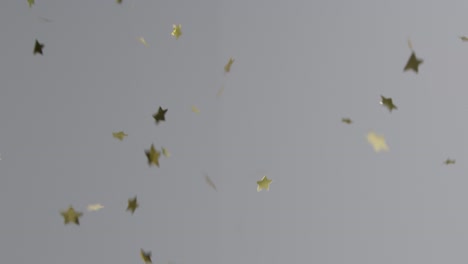 stationary shot of gold star confetti falling against a grey background