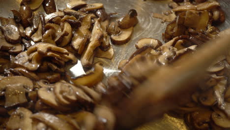 Macro-overhead-shot-of-mixing-fried-mushroom-slices-with-wooden-spoon