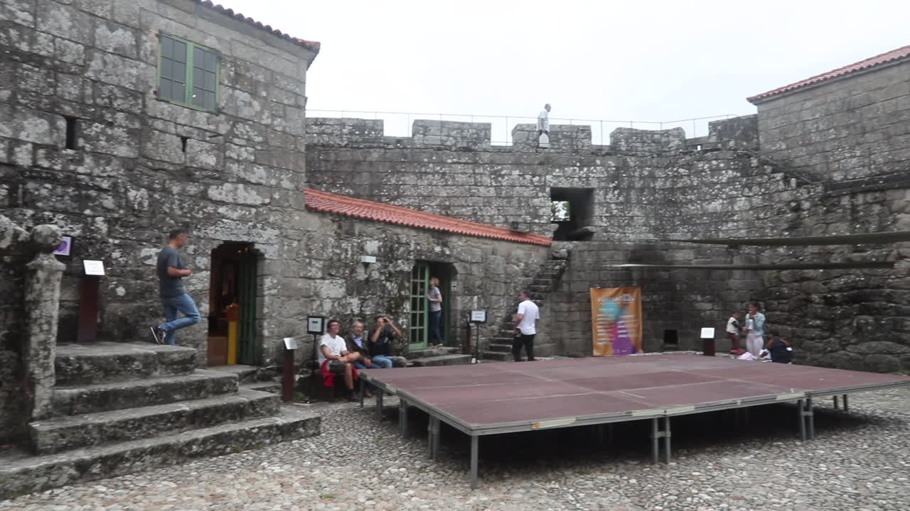 Tourists explore an old stone fortress with outdoor seating and raised platform for events