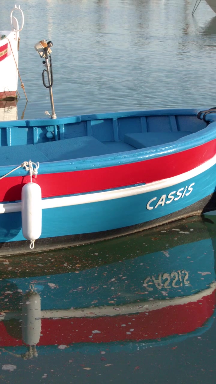 Inquadratura media statica di una colorata barca pointu in legno che galleggia in calme acque mediterranee.