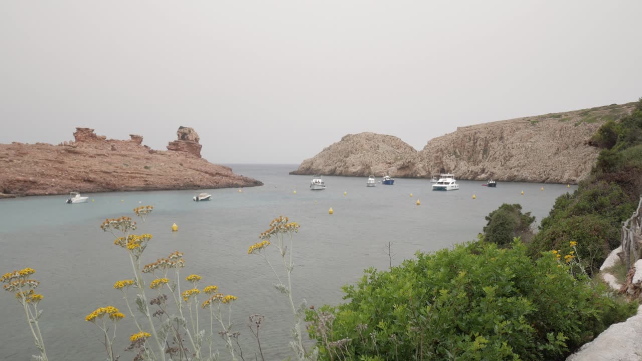 Secluded rocky cove in Cala Morell, Menorca, with boats floating in turquoise waters