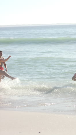 vertical video: diverse group of friends playing and splashing in ocean waves at beach