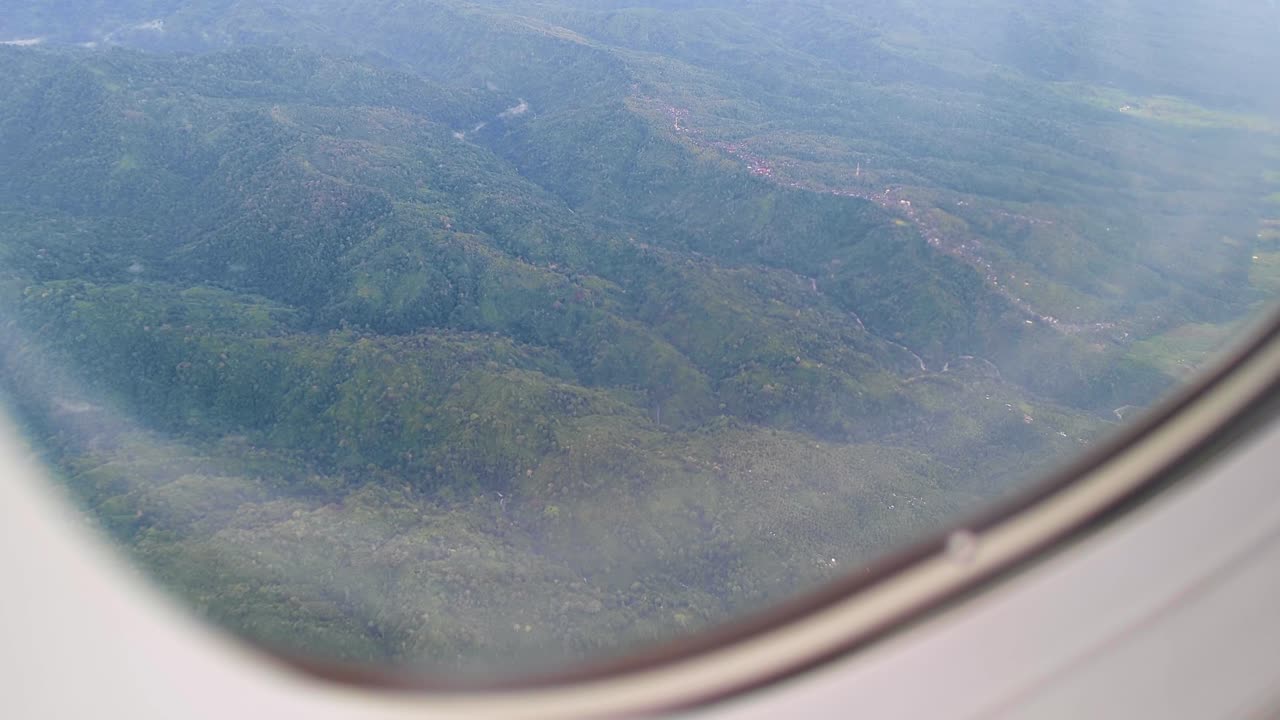 Aerial view from airplane window of rugged mountainous terrain and rural communities in Indonesia flying into tropical island of Bali
