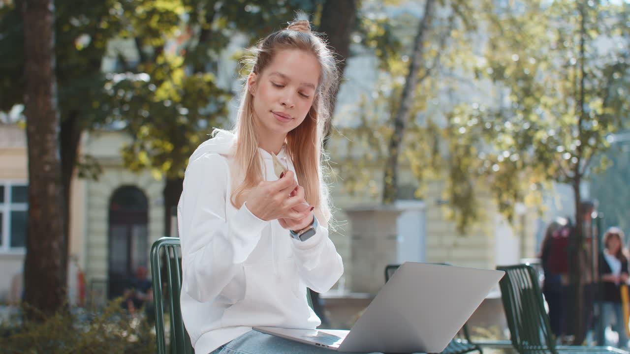 Happy young woman girl using credit bank card and laptop purchases online shopping on city street