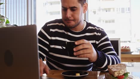 hombre usando una computadora portátil mientras toma una taza de café