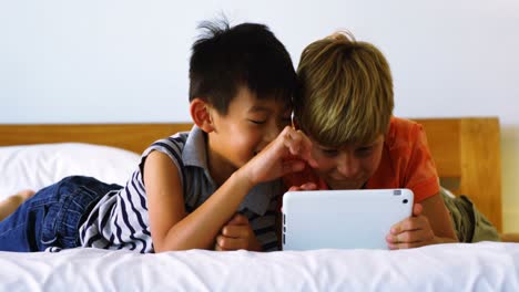 Siblings-using-digital-tablet-in-bedroom