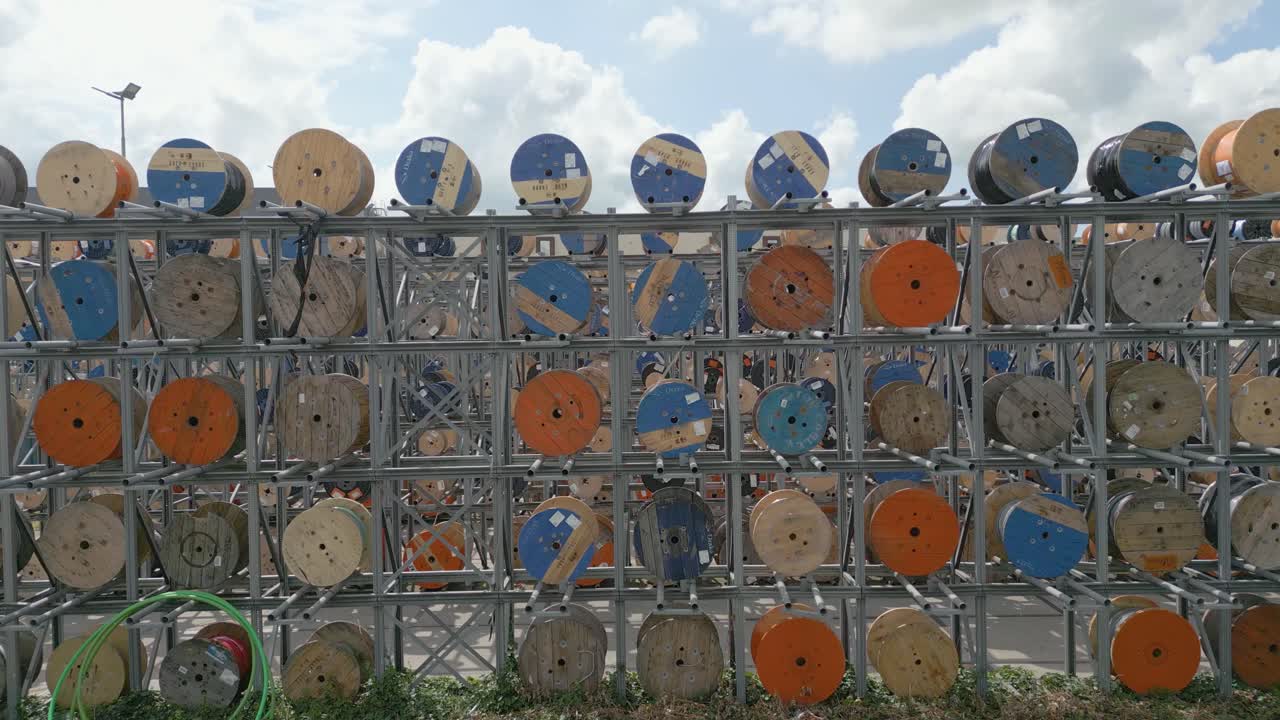 Side angle drone footage of colorful cable reels stacked in a symmetrical metal rack structure outdoors