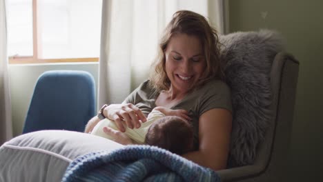 video of happy caucasian mother feeding newborn baby in armchair