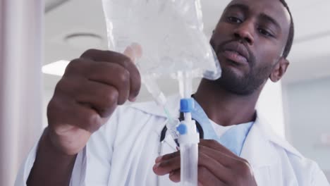 African-american-male-doctor-checking-drip-in-hospital-room,-slow-motion