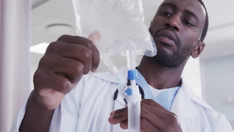 médico afroamericano chequeando el goteo en la habitación del hospital, cámara lenta