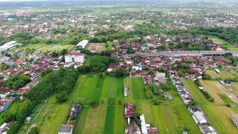 Vibrant-green-fields-and-Yogyakarta-outskirts,-aerial-drone-view