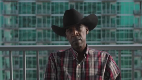 establishing shot of african american male with cowboy hat sitting on balcony as wind blows