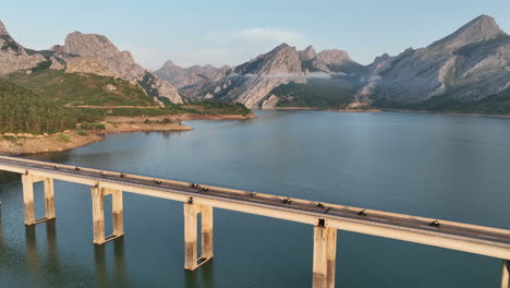 aerial cinematic drone shot following a group of motorcyclists heading out on a morning adventure crossing the riaño bridge at sunrise surrounded by the spectacular cantabrian mountains, leon, spain