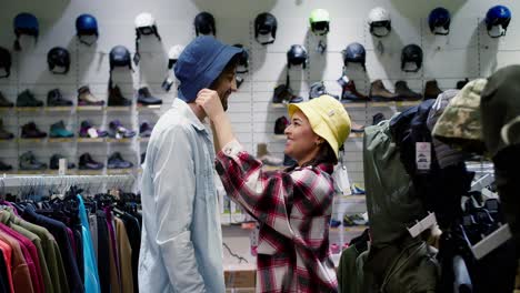 Una-Pareja-Joven-Disfruta-Y-Se-Divierte-Comprando-Juntos-El-Estilo-De-Vida-Al-Aire-Libre,-Ambos-Probando-Sombreros-De-Verano