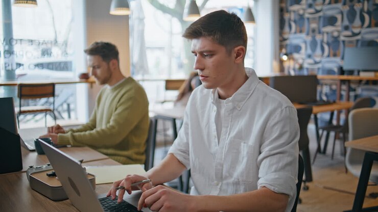 Selbstbewusster Freelancer arbeitet im Großraumbüro aus der Ferne, Nahaufnahme. Mann tippt auf Laptop