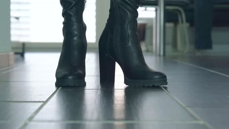 girl struts in front of the close up camera in black faux leather high heels block heel boots around