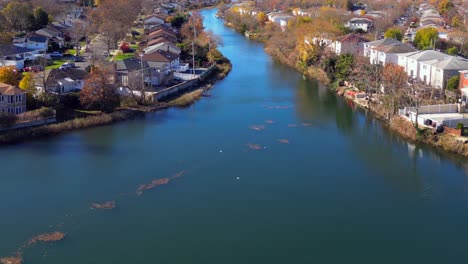 An-aerial-view-along-a-neighborhood-creek,-behind-houses-on-a-sunny-day