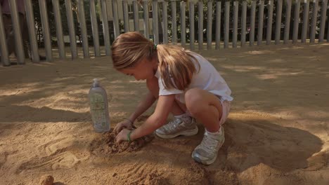 Little-girl-playing-in-a-playground,-making-constructions-with-sand-and-water
