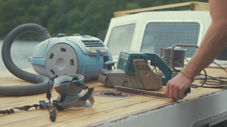 Carpenter setting up belt sander and hoover to sand wood boat roof planks
