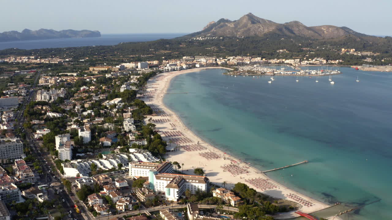 ciudad de alcudia con playa, puerto y península montañosa en mallorca