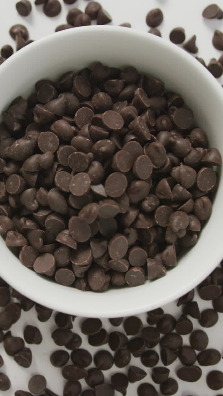 video de arriba de un cuenco de trozos de chocolate con una cuchara de madera sobre un fondo blanco