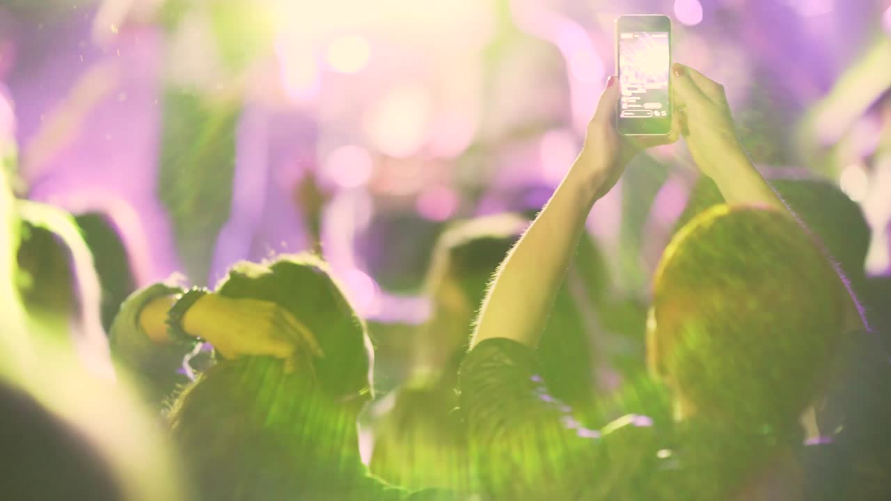 스마트워치 폰을 들고 음악 공연을 촬영하는 인식 할 수없는 사람들의 군중의 손에 무대에서 밝은 조명이 있습니다.