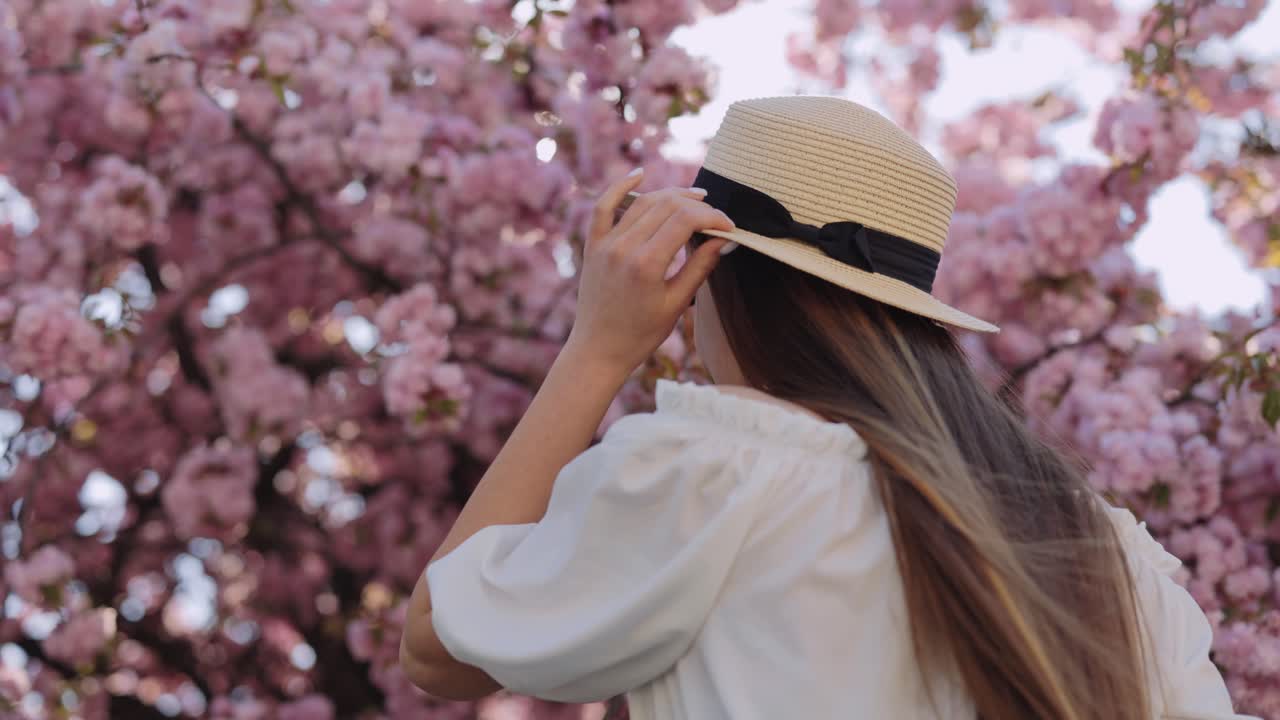 Woman wearing a straw hat amidst cherry blossoms