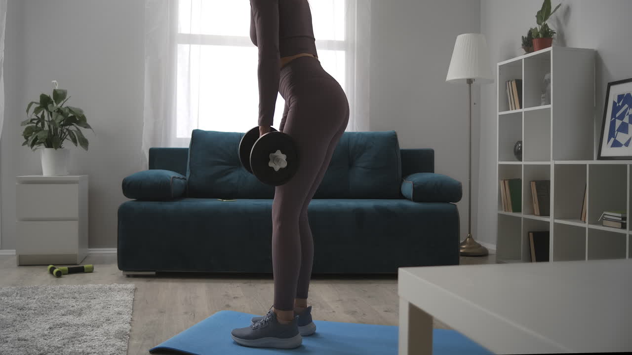 beautiful woman is training with dumbbells in hands leaning forward with weight workout in living room healthy lifestyle and bodybuilding at home