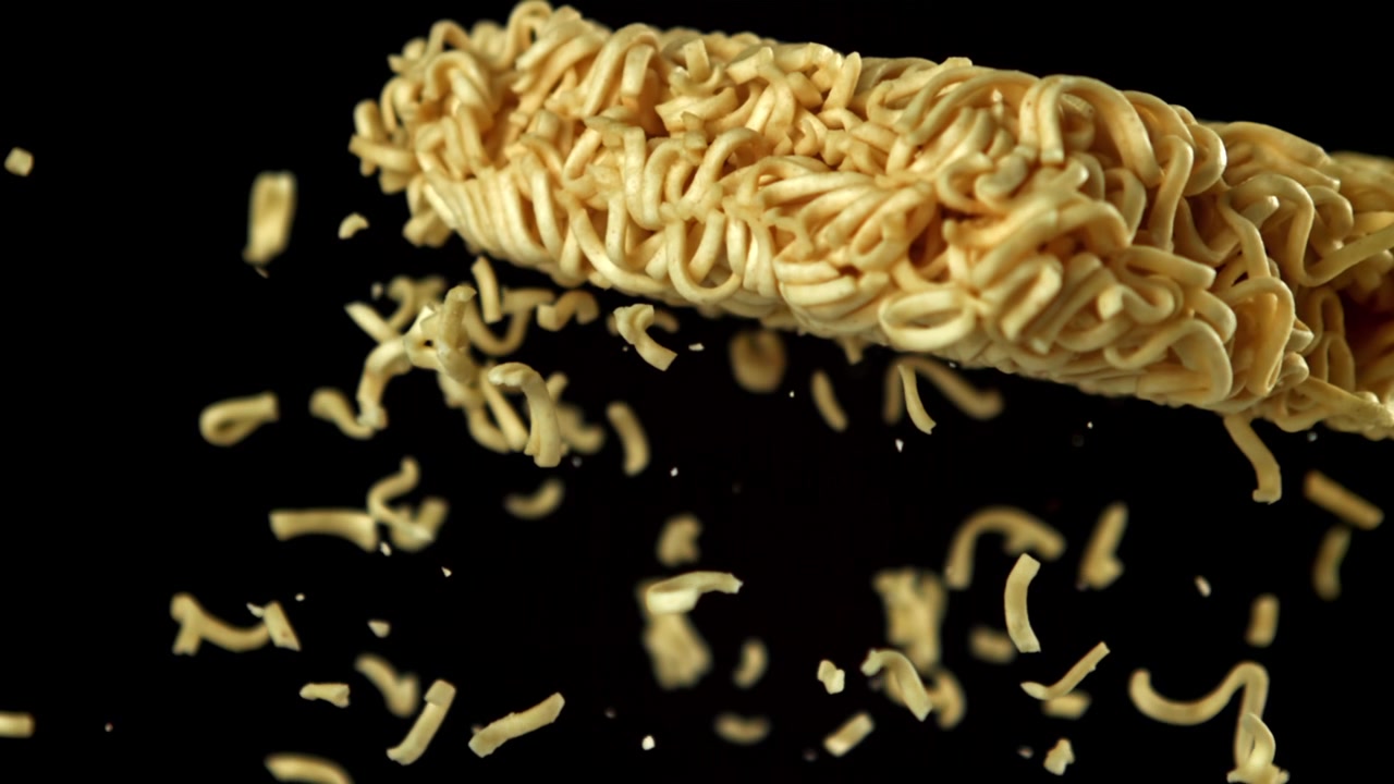 Noodles istantanei che si rompono e cadono al rallentatore su sfondo nero