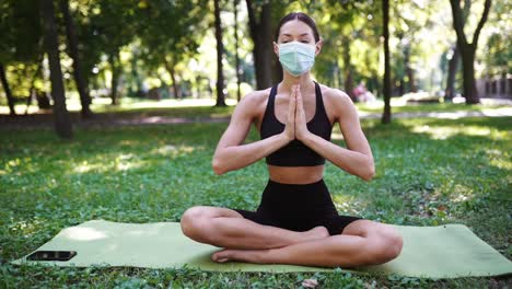 mujer meditando en un parque durante una pandemia con una máscara