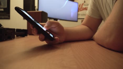 man scrolling social media feed on his mobile phone with animated screen saver on desktop computer in the background