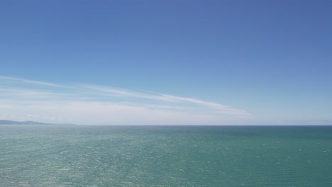 Slow-aerial-ascent-and-reverse-above-beautiful-ocean-on-a-sunny,-windy-day-with-shadows-and-patterns-on-water---Pegasus-Bay,-New-Zealand