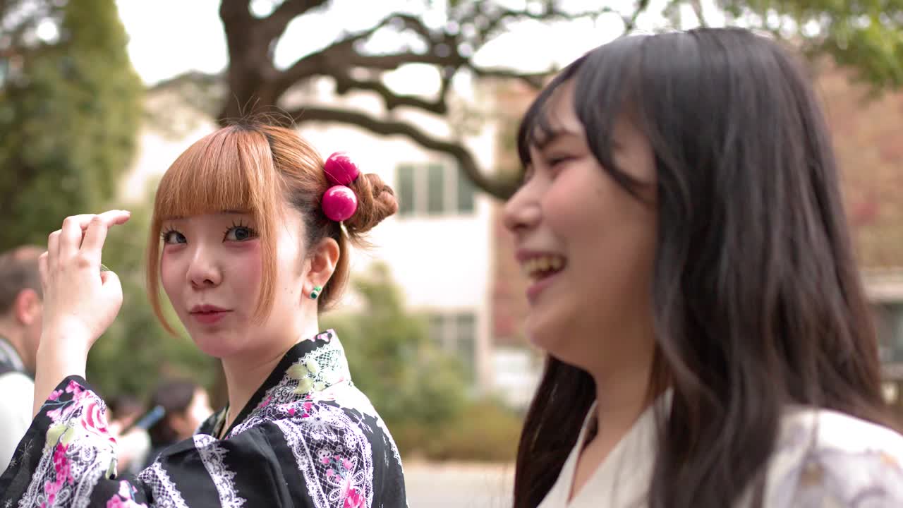 日本の東京で、伝統的な着物と浴衣姿の若い女性二人が屋外で談笑している