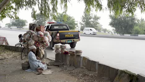 a delightful photo of a handmade hotpot vendor sitting by the roadside! in the background, a police car, while cars pass by