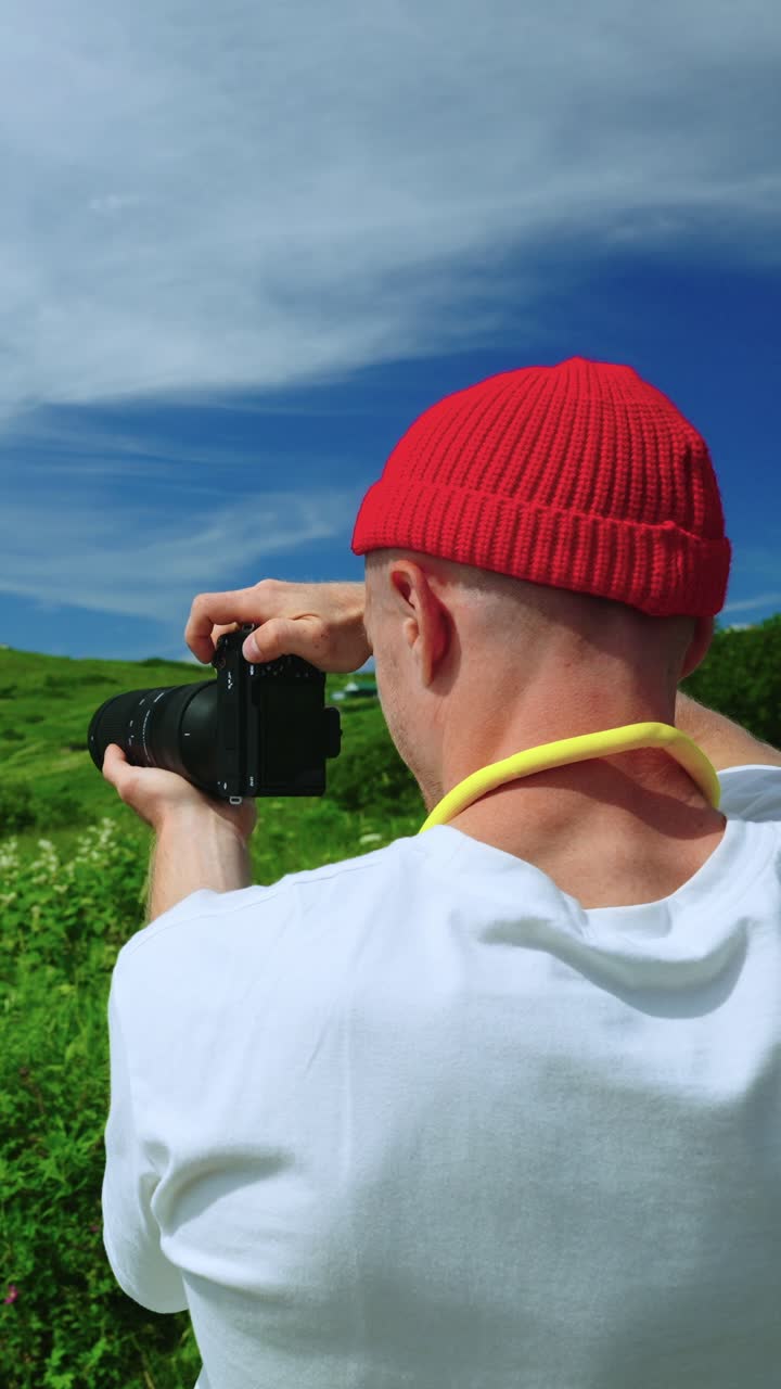 Uomo con berretto rosso che fotografa un paesaggio verde