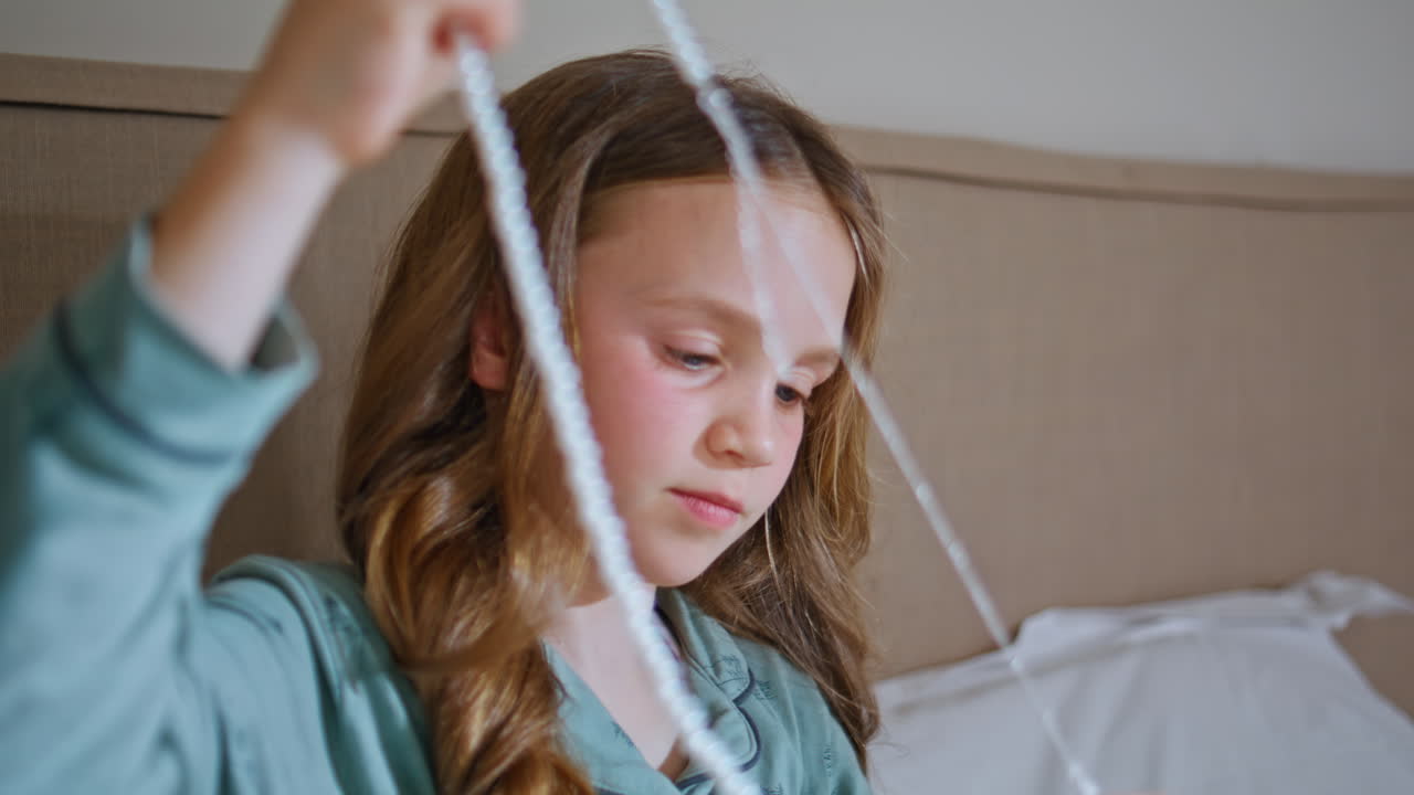 Closeup girl examining jewellery in bedroom. Smiling small kid admiring necklace