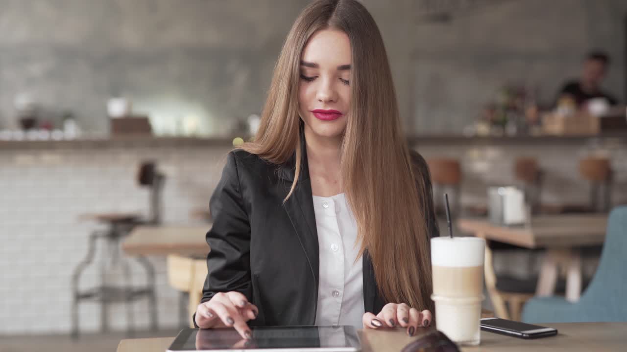 Bella giovane donna ascolta musica dal suo smartphone mentre lavora sul suo tablet in un caffè.