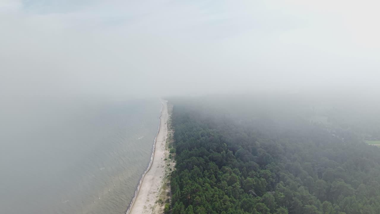 Coastal road disappears into dense low clouds, fog blankets land in moody aerial