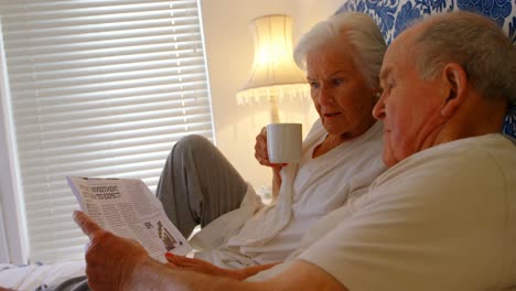 side view of caucasian senior couple reading news paper on bed in bedroom at comfortable home 4k