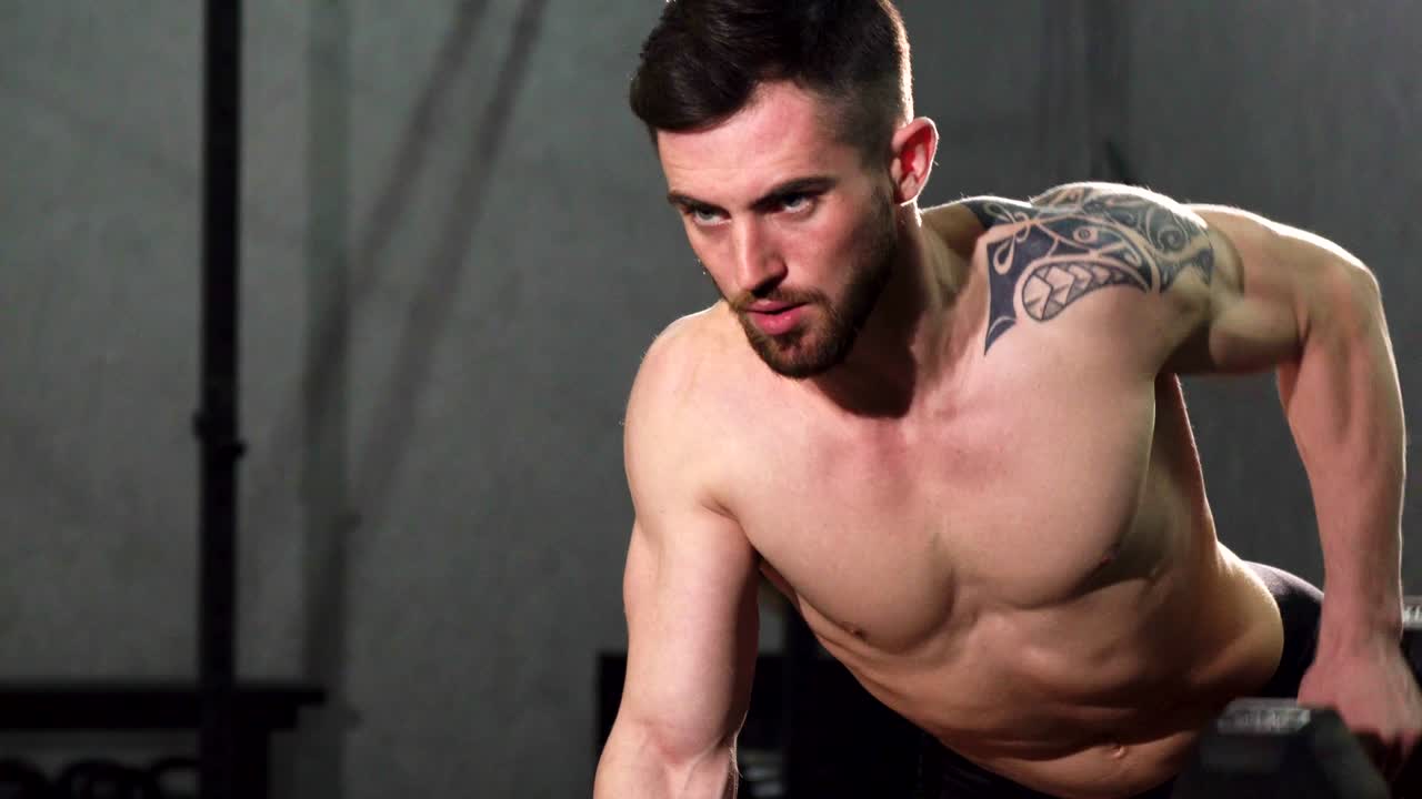 Focused young shirtless male athlete doing back workout at the gym