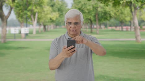 Indian-old-man-scrolling-through-phone-in-park